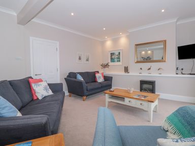 A living room with two dark grey sofas a light blue armchair a wooden coffee table and a wall-mounted television at Moorings in Kingswear Devon