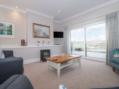 A living room with a coffee table and armchairs next to sliding glass doors opening to a balcony with a view at Moorings in Kingswear Devon