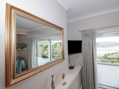 A wall with a large framed mirror reflecting a room with sliding glass doors and a view of hills at Moorings Kingswear Devon