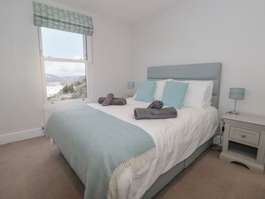A bedroom with a double bed with blue pillows and blanket next to a window overlooking a hill at Moorings in Kingswear Devon