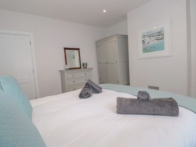 A bedroom with a bed with rolled towels a dresser with mirror a wardrobe and a framed picture on the wall at Moorings in Kingswear Devon