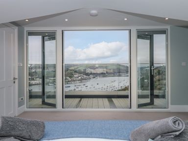 A bedroom with glass doors opening to a balcony overlooking a harbor with boats at Moorings in Kingswear Devon
