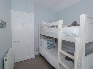 A bedroom with white bunk beds pillows and towels near a white door and radiator at Moorings in Kingswear Devon