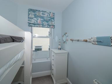 A small bedroom with bunk beds a white chest of drawers and a window with a sailboat-patterned blind at Moorings in Kingswear Devon