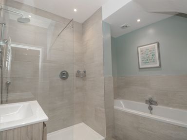 A bathroom with a walk-in shower sink and bathtub with fish artwork on the wall at Moorings in Kingswear Devon