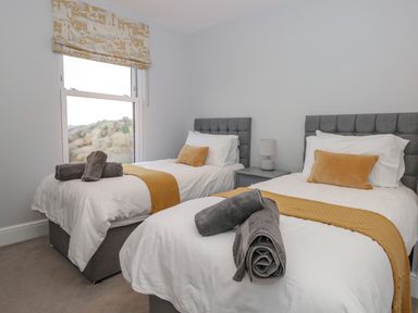 A bedroom with two single beds with yellow throws and gray towels at Moorings in Kingswear Devon