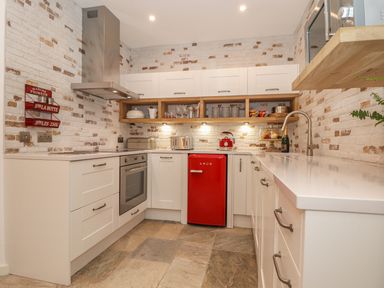 A kitchen with white cabinets a red mini fridge a stainless steel oven and hood and open shelves with dishes at Beach Hut in Trebarwith Strand