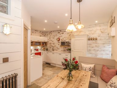 A kitchen with white cabinets wooden table flowers in a vase and bench seating at Beach Hut in Trebarwith Strand
