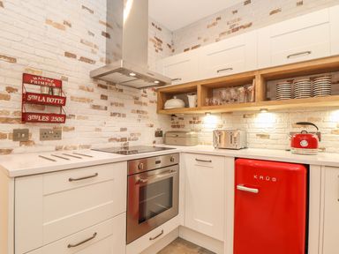 A kitchen with white cabinets a red fridge a stainless steel oven a stovetop a toaster and a kettle at Beach Hut in Trebarwith Strand