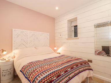 A bedroom with a bed covered by a multicolored blanket white wooden paneled walls and two bedside tables with lamps at Beach Hut in Trebarwith Strand