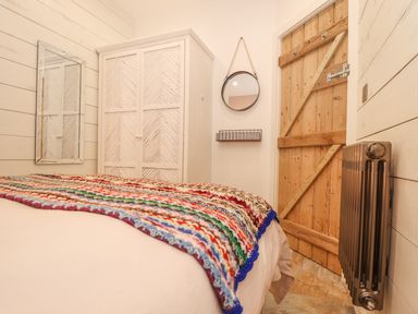 A bedroom with a wooden door a metal radiator a white wardrobe a rectangular mirror and a round mirror with a wire shelf at Beach Hut in Trebarwith Strand