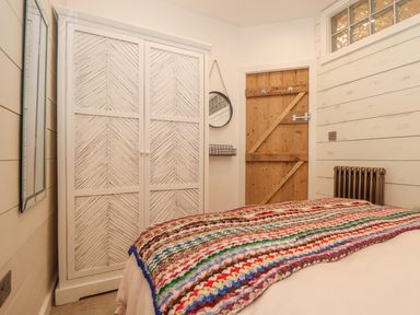 A bedroom with a colorful blanket on the bed a white wardrobe a round mirror a wooden door and a wall radiator at Beach Hut in Trebarwith Strand