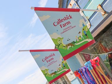 Two flags advertising Callestick Farm Champion Cornish Ice Cream outside a shop with beach toys on display at Beach Hut in Trebarwith Strand