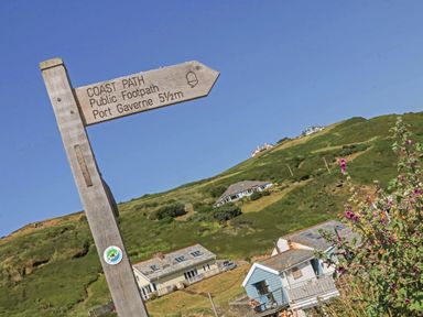 A wooden signpost for the coast path public footpath on a hill with houses and green vegetation