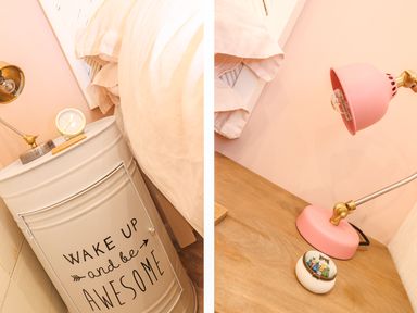 A bedside table with a clock and lamp beside a bed and another wooden bedside table with a pink lamp and small decorative box at Beach Hut in Trebarwith Strand