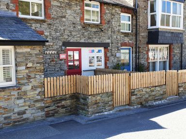 Stone exterior of a building with a red door and blue door with wooden picket fences in front at Beach Hut in Trebarwith Strand