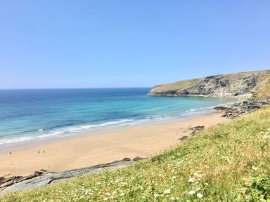 A sandy beach with a few people walking near the shoreline and cliffs in the background at Beach Hut in Trebarwith Strand