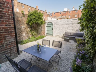 An outdoor patio area with a table, chairs, a sofa, gravel ground and plants at West Cliff Apartment in Whitby