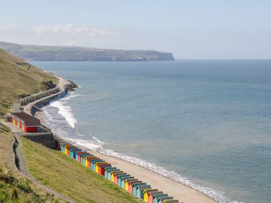 A coastline with colorful beach huts along a pathway beside the sea at West Cliff Apartment in Whitby