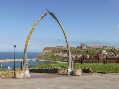 A whale bone arch overlooking a coastal town with benches and a ruined abbey in Whitby