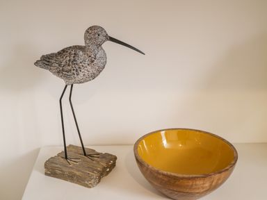 A wooden bird sculpture on a stand next to a wooden bowl with a yellow interior at West Cliff Apartment in Whitby