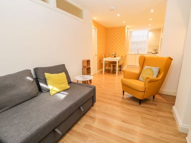 A living area with a gray sofa and yellow armchair next to a small white table and a dining table in the background at West Cliff Apartment in Whitby