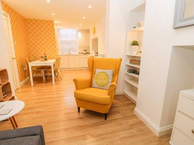 An open living space with a yellow armchair a white dining table with chairs and a kitchen area at West Cliff Apartment in Whitby