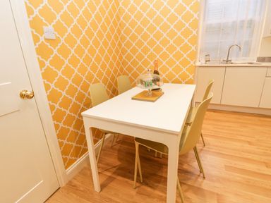 A kitchen dining area with a white table and four chairs and a yellow patterned wallpaper at West Cliff Apartment in Whitby