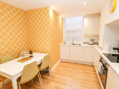 A kitchen with a white dining table and chairs beside a yellow patterned wall at West Cliff Apartment in Whitby