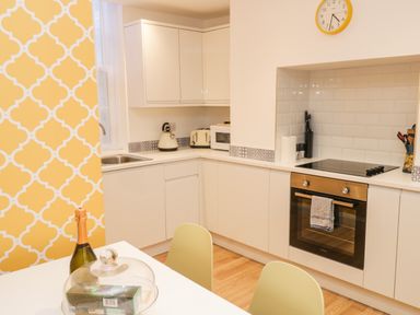 A kitchen with white cabinets a built-in oven a microwave a toaster kettle and a dining table with chairs at West Cliff Apartment in Whitby
