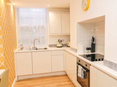 A kitchen with white cabinets a stainless steel sink a kettle toaster stove oven and a yellow patterned wall at West Cliff Apartment in Whitby