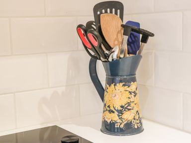 A dark blue jug with yellow flowers holding kitchen utensils on a white countertop in a kitchen at West Cliff Apartment in Whitby