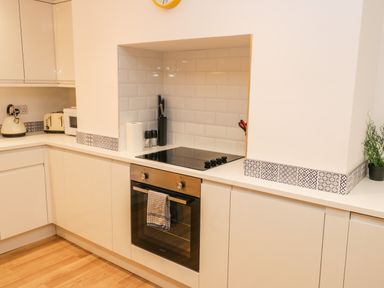A kitchen with white cabinets an oven a stovetop a kettle a toaster and a plant at West Cliff Apartment in Whitby