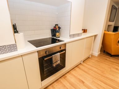 A kitchen area with an electric cooktop and oven a kitchen towel hanging on oven door and utensils in a container on the counter at West Cliff Apartment in Whitby