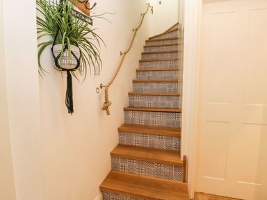 A staircase with patterned risers wooden treads and a rope handrail a hanging plant on the wall at West Cliff Apartment in Whitby