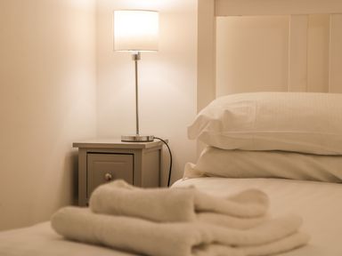 A bedside table with a lamp next to a bed with pillows and folded towels at West Cliff Apartment in Whitby