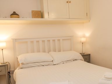A bedroom with a white bed and two pillows two bedside tables with lamps and a cabinet above the bed at West Cliff Apartment in Whitby