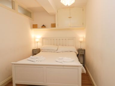 A bedroom with a double bed two bedside tables and lamps and a shelf with decorative items at West Cliff Apartment Whitby