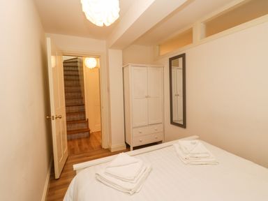 A bedroom with a bed with folded towels a white wardrobe a wall mirror and a door leading to a staircase at West Cliff Apartment Whitby