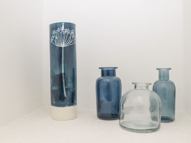 A set of four blue and clear glass vases on a white surface in a corner