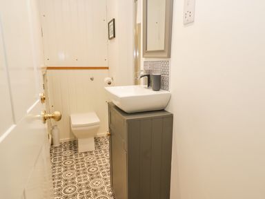 A small bathroom with a toilet a sink on a cabinet patterned floor tiles and white paneled walls at West Cliff Apartment in Whitby