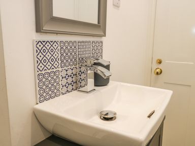 A white ceramic sink with a chrome faucet and patterned tiles on the wall above it at West Cliff Apartment in Whitby