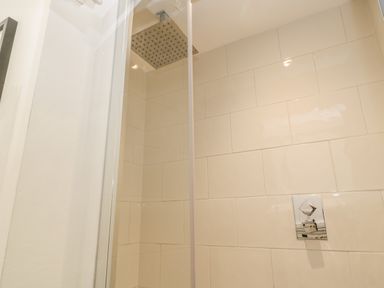 A shower area with beige tiles a square shower head and a control handle at West Cliff Apartment Whitby