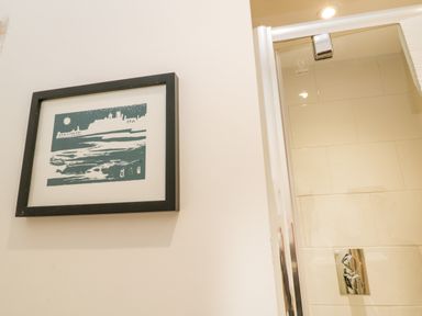 A framed artwork on a wall next to a glass shower door in a bathroom at West Cliff Apartment in Whitby