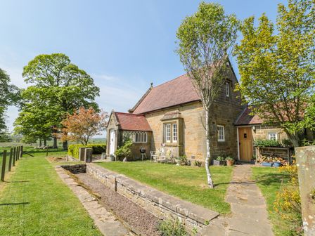 A stone cottage with a red tiled roof surrounded by green grass trees and a stone pathway at Fenwick Retreat at Fenwick Lodge in Fenwick near Ponteland