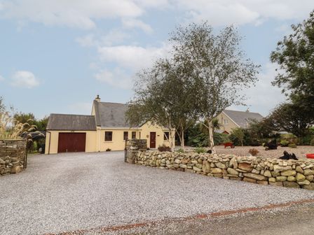 A gravel driveway leading to a house with a garage and stone wall with trees in the garden at Silver Birch in Dromelihy Cooraclare County Clare