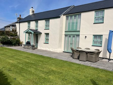 A backyard with patio furniture and grass outside a house with green window frames at Tyn Y Buarth in Dyffryn Ardudwy