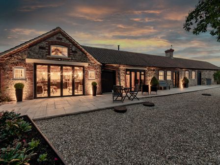 Exterior of a long stone building with large windows and outdoor seating at Sykes Lodge in Malton