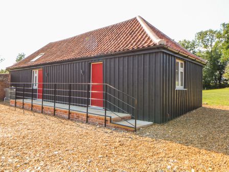 A black wooden barn with two red doors a ramp and gravel ground at Sparrow Barn in Reepham