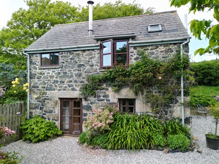 A stone cottage with windows and plants in a garden at Higher Lampra in Mullion